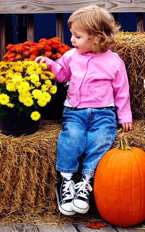 Little girl with fall flowers, haybale and pumpkin